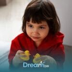Autistic girl in red robe holding two toy ducks, showing focused and thoughtful expression during independent play time