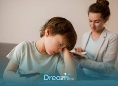 Autistic boy looking frustrated while drawing, resting head on hand as adult in background observes & provides gentle support