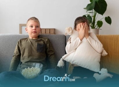 Two autistic kids sitting on couch watching TV, one calmly eating popcorn while the other hides face with pillow