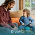 Therapist and autistic boy sit on carpet at home, joyfully playing instruments, smiling, & engaging in playful interaction.