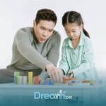 Therapist & autistic girl building with colorful blocks at a table, focusing on problem-solving & cooperative play at home