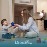 Therapist interacting with autistic toddler on the floor using a toy helicopter while another parent prepares food