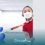 Autistic girl wearing face mask peeking from behind wall near syringe, representing common vaccine concerns and autism.