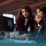 Two therapist collaborating at desk reviewing code and data on computer screen during hands-on technical training session