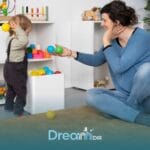 Therapist sitting on the floor encouraging an autistic toddler to play with colorful balls, supporting sensory & motor skill