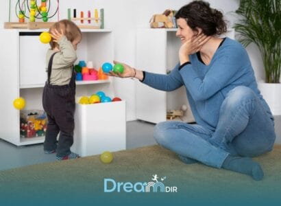 Therapist sitting on the floor encouraging an autistic toddler to play with colorful balls, supporting sensory & motor skill