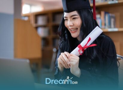 ABA graduate in cap and gown holding diploma while attending virtual ceremony on laptop in a quiet indoor setting