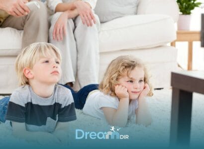 Two young autistic children lie on a soft carpet watching television together while parents relax in the background at home