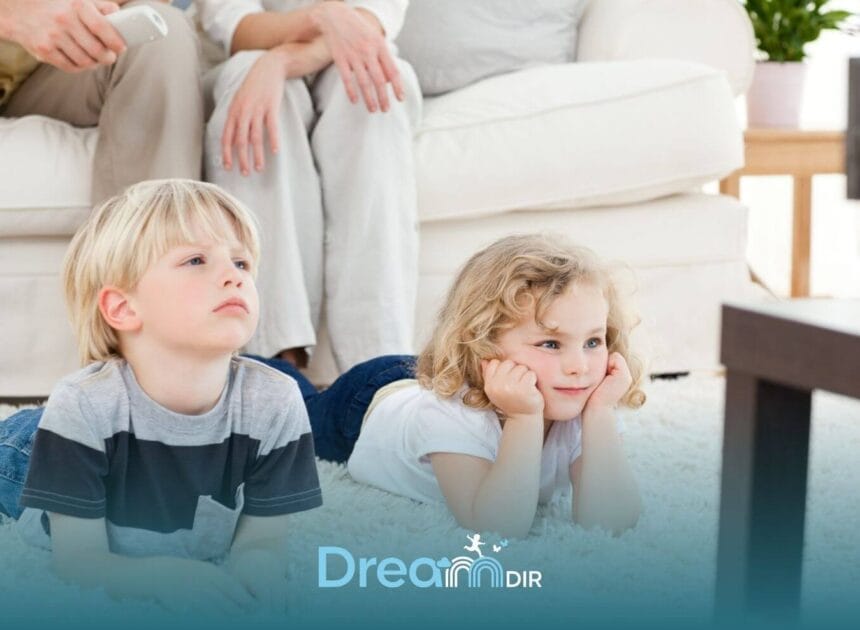 Two young autistic children lie on a soft carpet watching television together while parents relax in the background at home