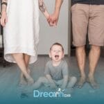 Therapists holding hands behind an autistic toddler sitting on the floor with toys, representing support & safety