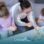 Therapist & two autistic children painting decorative eggs together at a table, promoting creativity & bonding