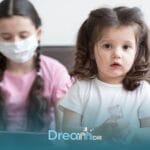 Autistic girl holding a bottle while caregiver wearing a mask uses a tablet during a pediatric therapy or assessment session
