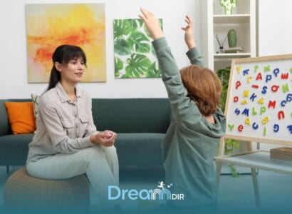 Autistic boy raises hands during a sensory integration therapy activity while therapist sits nearby during therapy