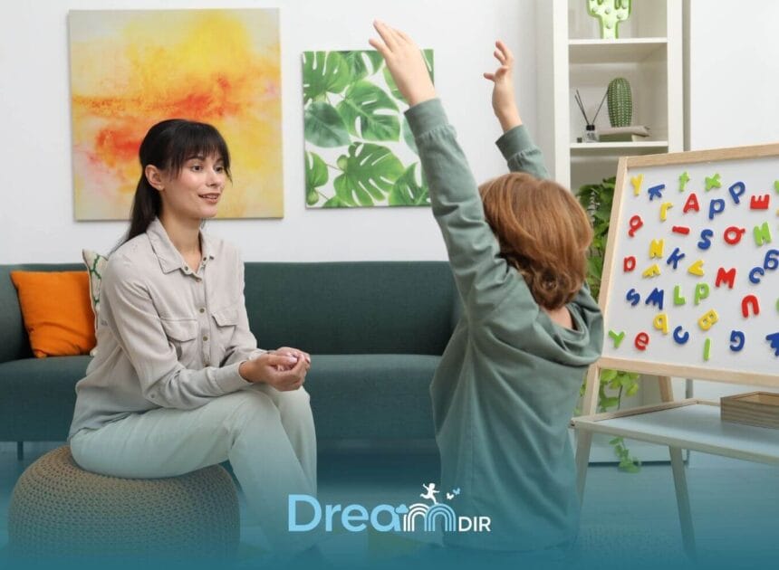 Autistic boy raises hands during a sensory integration therapy activity while therapist sits nearby during therapy