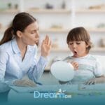 Speech therapist helps an autistic young boy practice mouth sounds and pronunciation using a mirror during a therapy session
