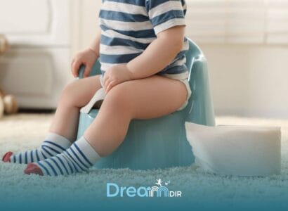 Autistic boy wearing striped socks sits on a potty training chair beside a roll of toilet paper in a bright home setting